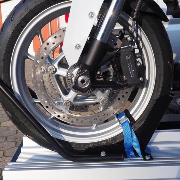 SMV Alu-Star Rolli. Das Vorderrad eines Motorrades gesichert mit Wippe, Reifenhaltebügel und Spanngurt auf der Plattform.