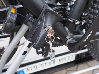 SMV Alu-Star Rolli – Zubehör Diebstahlsicherung. Schloß mit steckendem Schlüssel am Fahrradhalter. Darin ist ein Fahrrad am Rahmenrohr gesichert.
